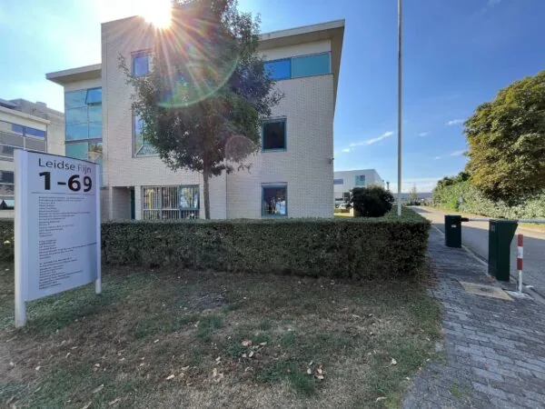 Kantoorgebouw in Leidse Rijn met zonlicht en een bord met huisnummers 1-69 bij de ingang.